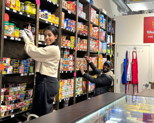 Two people interacting with a shelf stocked with various products in a store setting.